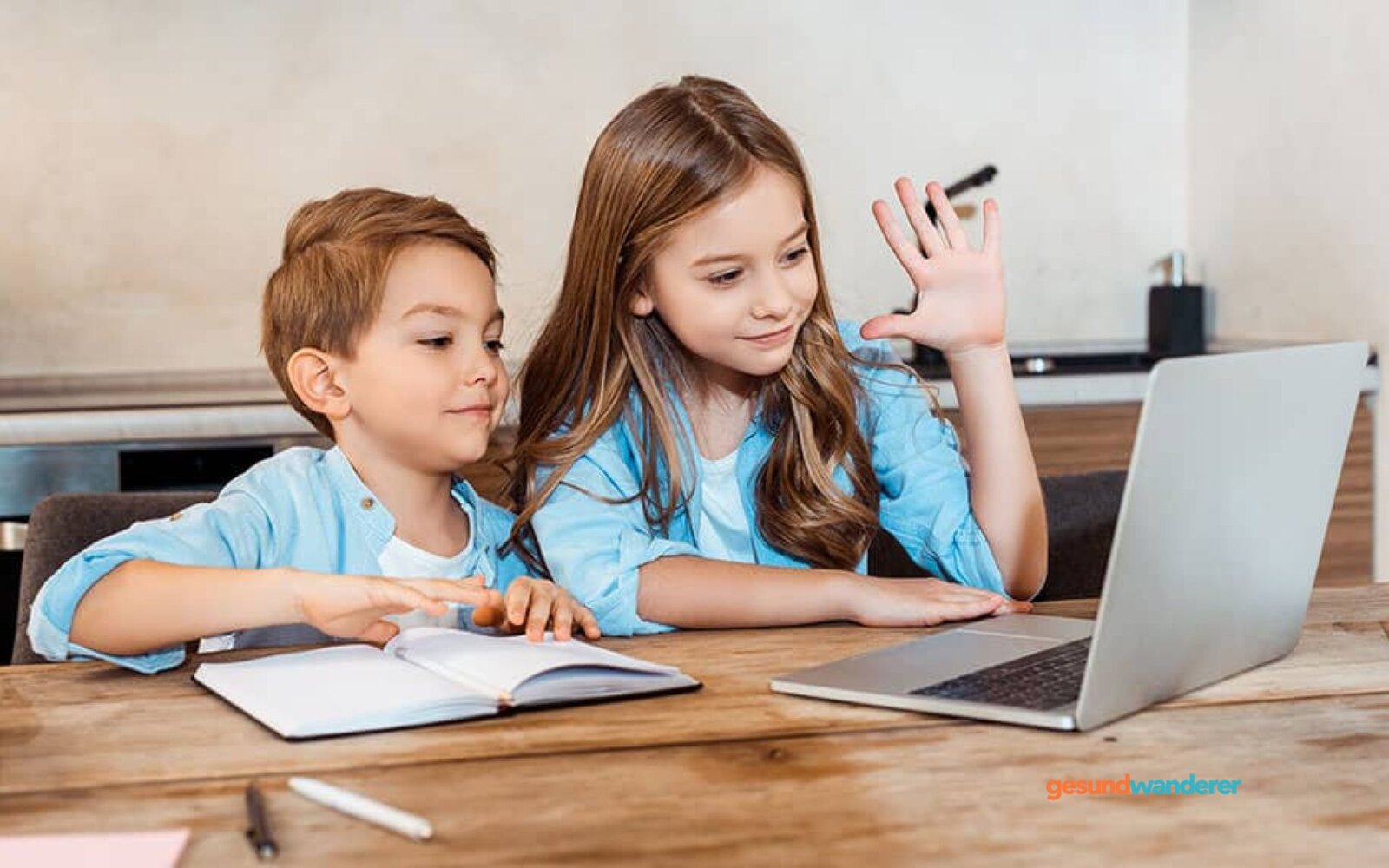 Zwei Kinder lernen gemeinsam am Laptop mit aufgeschlagenem Heft