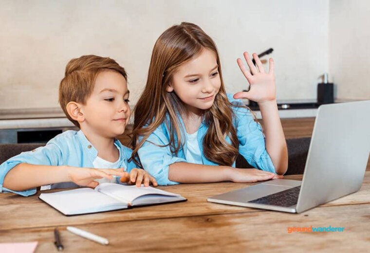 Zwei Kinder lernen gemeinsam am Laptop mit aufgeschlagenem Heft