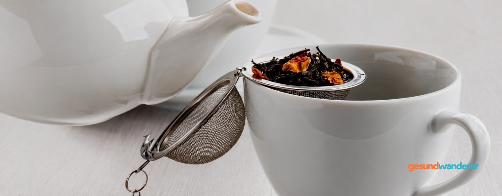 Teesieb mit loser Teemischung auf einer weißen Tasse neben einer Teekanne